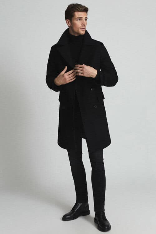 Men's smart all black outfit of turtleneck, jeans and overcoat with Chelsea boots