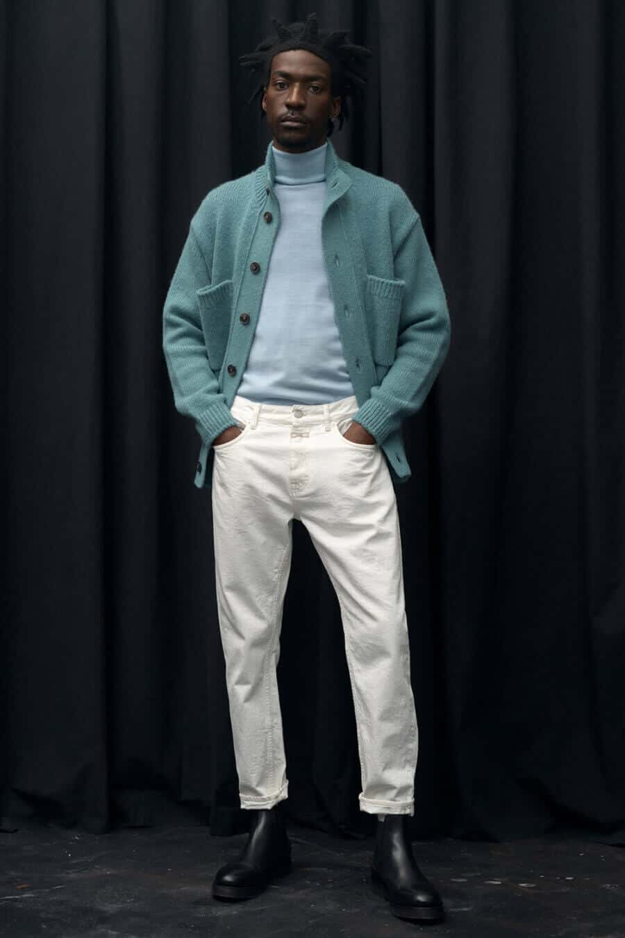Men's tonal blue turtleneck and cardigan outfit with white jeans and boots