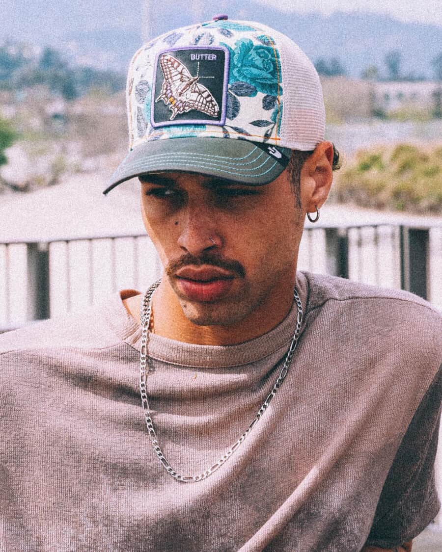 Black man wearing a washed heavyweight T-shirt, silver neck chain and Goorin Butterfly baseball cap