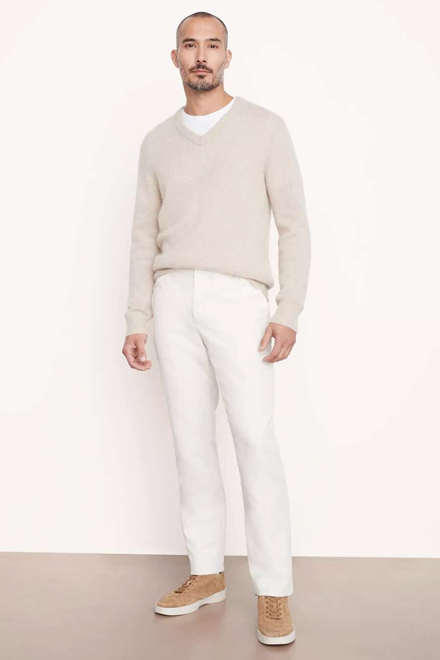 Men's white pants, white T-shirt, beige V-neck sweater and tan suede sneakers outfit