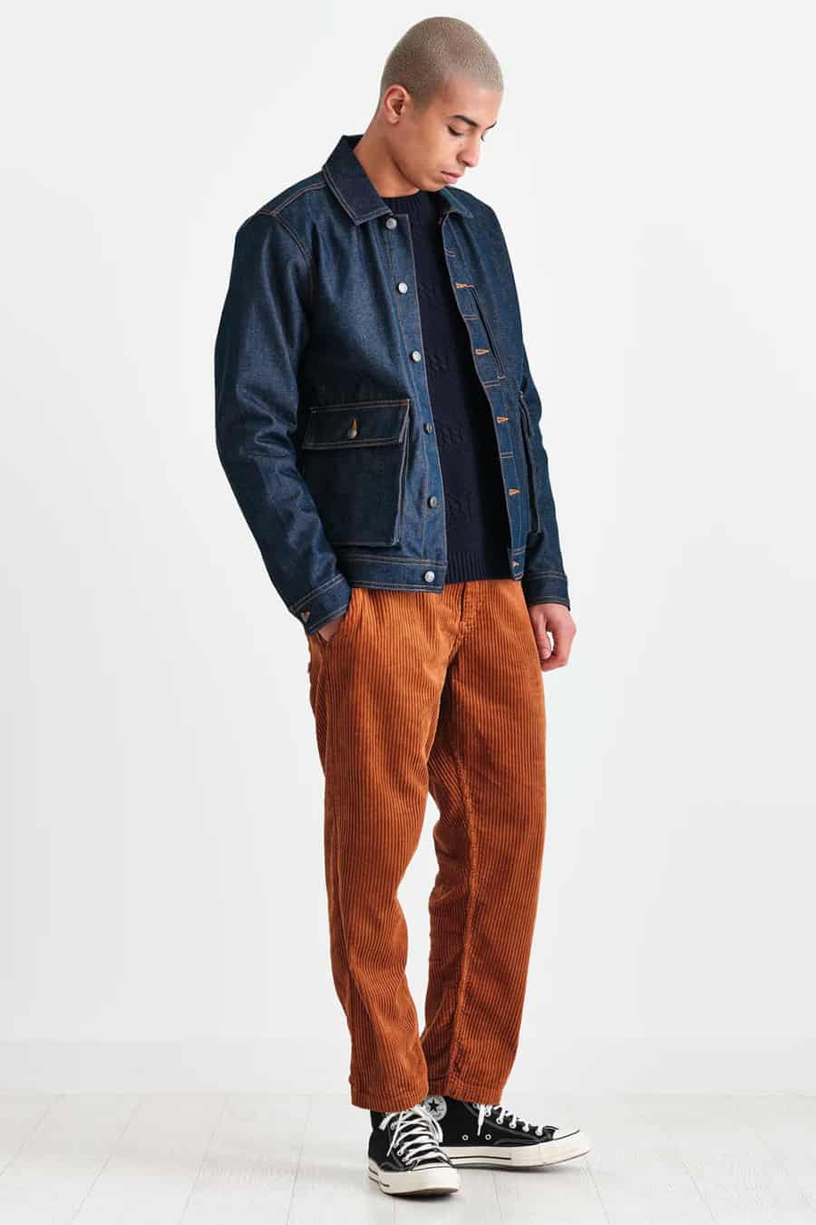 Men's brown-orange corduroys, navy sweatshirt, raw denim jean jacket and black canvas high-tops outfit