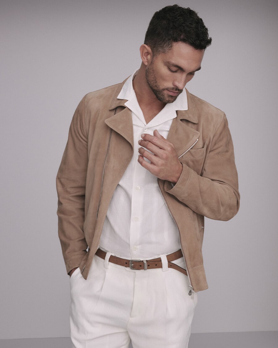 Man wearing Brunello Cucinelli white pleated pants, white camp collar shirt, tan suede belt and caramel suede biker jacket