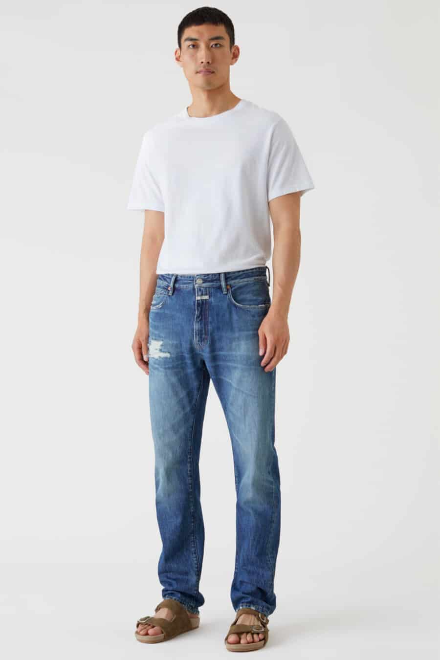 Men's subtly distressed blue jeans, white tucked in T-shirt and sandals outfit