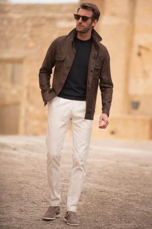 ITalian man wearing white pants, black top, brown safari shirt, grey suede loafers and tortoiseshell sunglasses