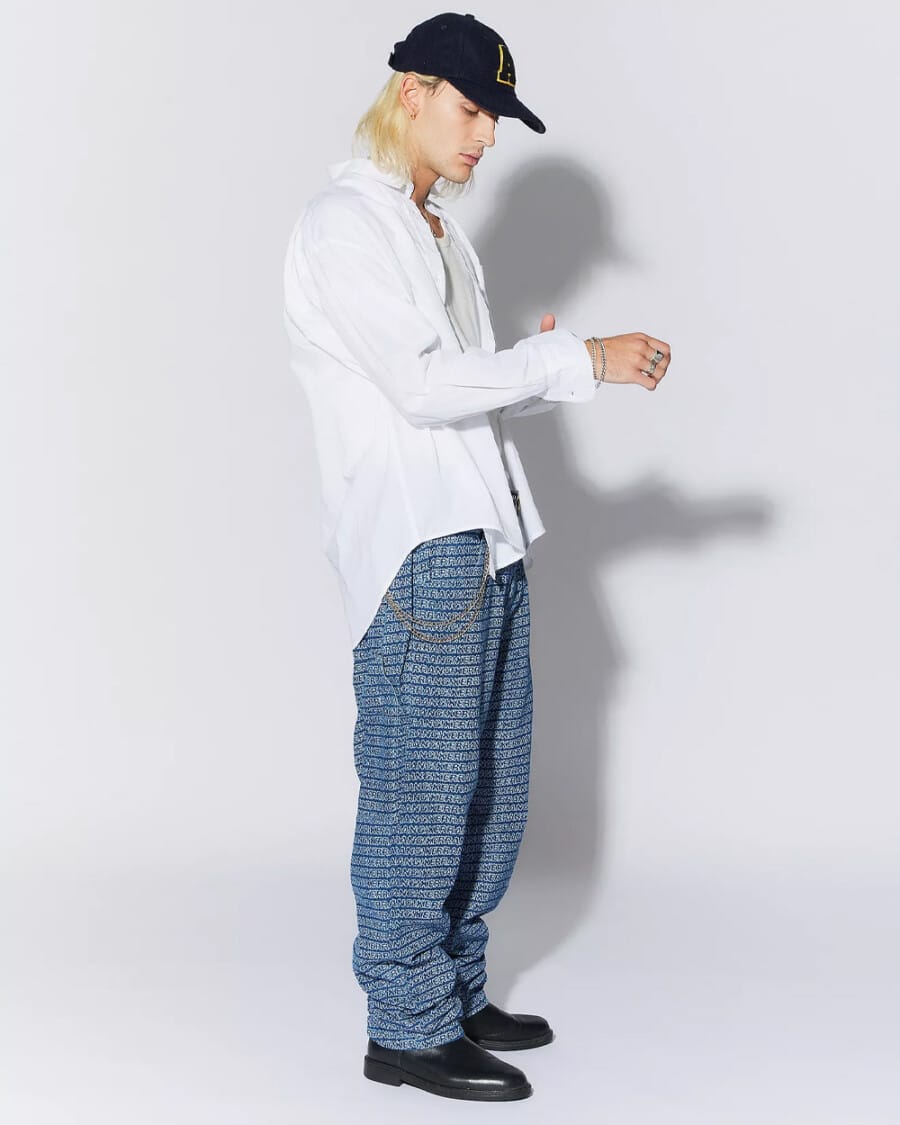 Men's printed jeans, off-white tank top, white open shirt, navy baseball cap, silver wallet chain and black Chelsea boots outfit
