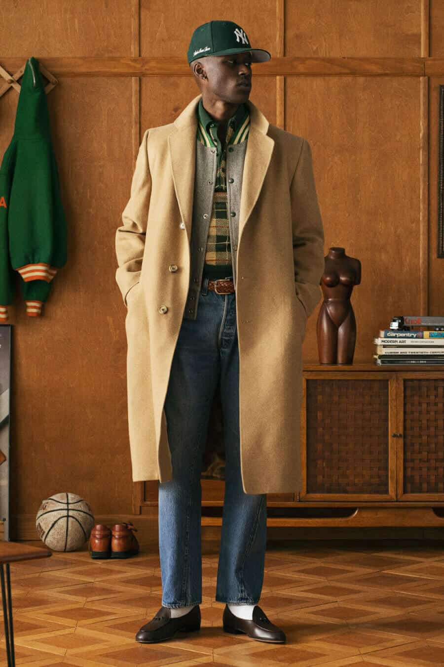 Men's preppy outfit with polo shirt, varsity jacket, overcoat and light wash jeans with loafers