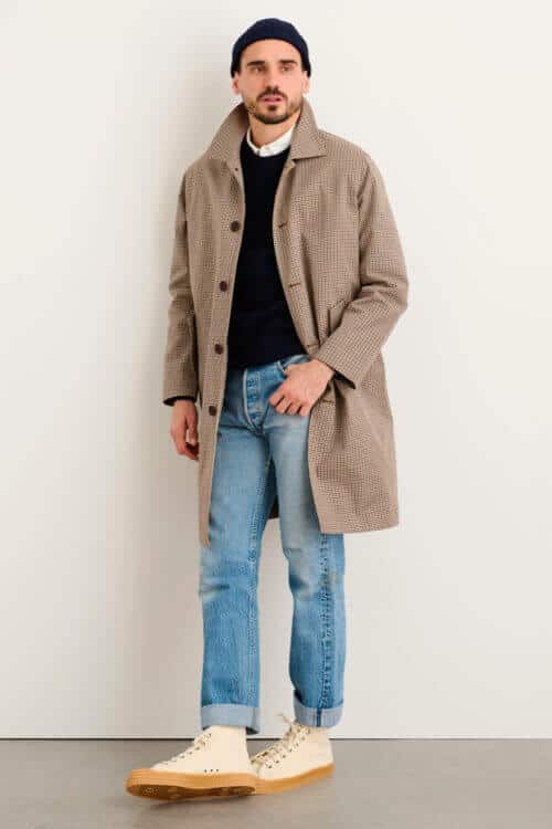 Men's light wash blue jeans, white shirt, navy sweater, tan check coat, navy beanie and off-white gum sole high-top sneakers outfit