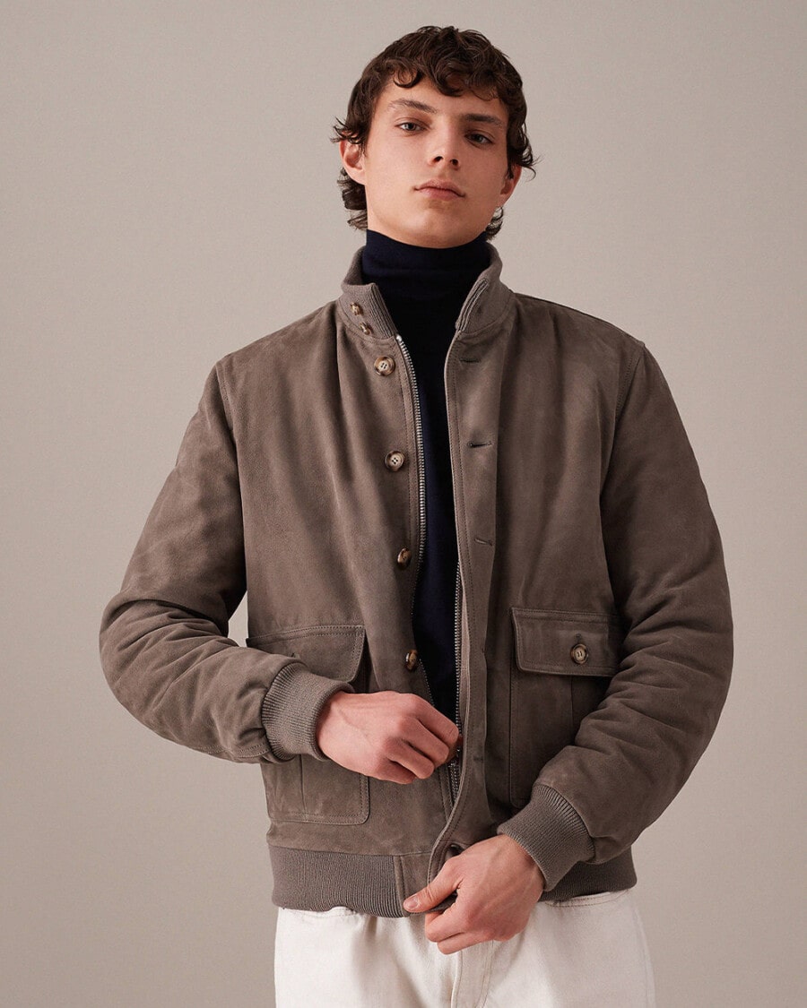 Man wearing a Valstar suede Valstarino bomber jacket with navy turtleneck and white jeans