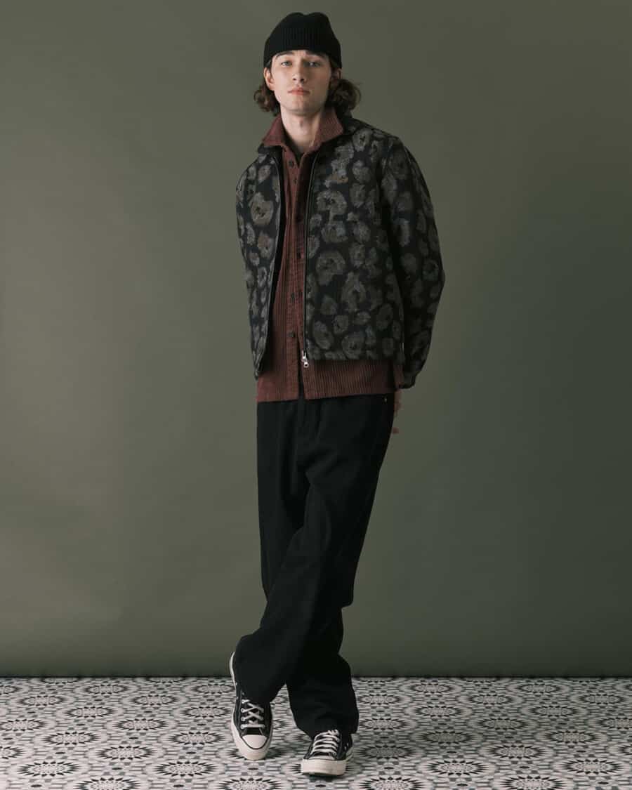 Men's loose black jeans, brown cardigan, patterned Harrington jacket and Converse sneakers outfit