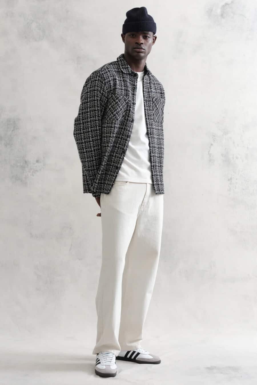 Men's off-white jeans, white T-shirt, black and grey checked overshirt, black beanie and Adidas Samba sneakers outfit