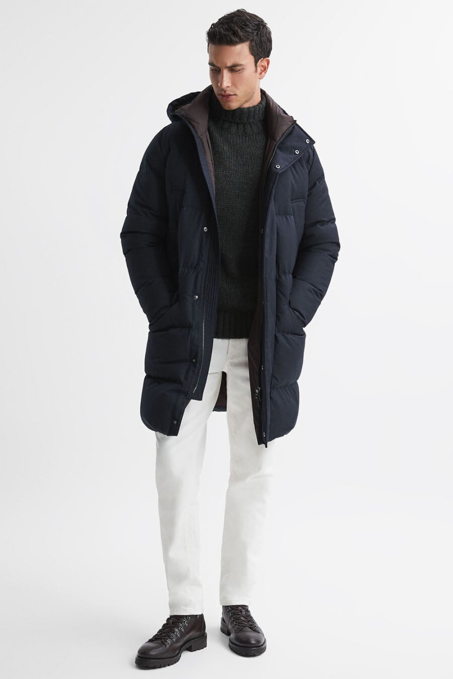Men's white jeans, chunky charcoal turtleneck, navy long puffer jacket and brown leather hiking boots outfit