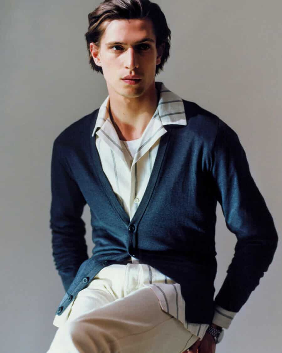 Male model Edoardo Sebastianelli wearing a white and blue stripe shirt, white pants and a navy cardigan