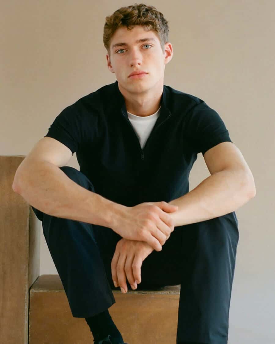 Male model Valentin Humbroich wearing black pants, a white T-shirt and black short sleeve shirt