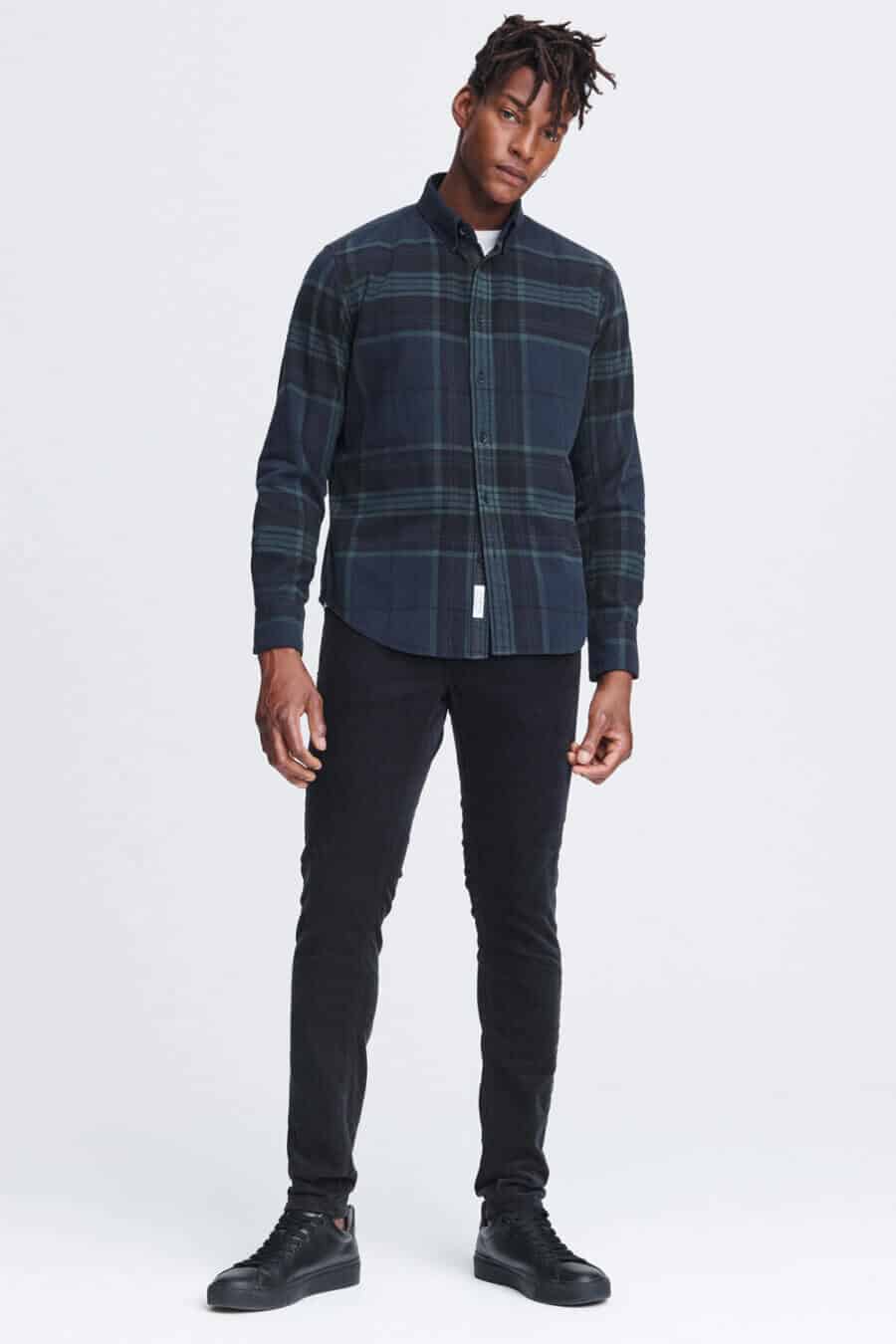 Men's black jeans worn with a black watch tartan flannel shirt and black sneakers