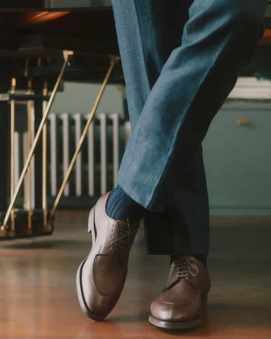 Man wearing brown leather Edward Green Derby shoes on feet with grey tailored pants and navy ribbed socks