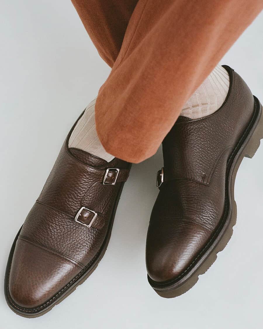 Man wearing luxury John Lobb brown pebble leather double monk-strap shoes on feet with beige socks and tan brown tailored pants