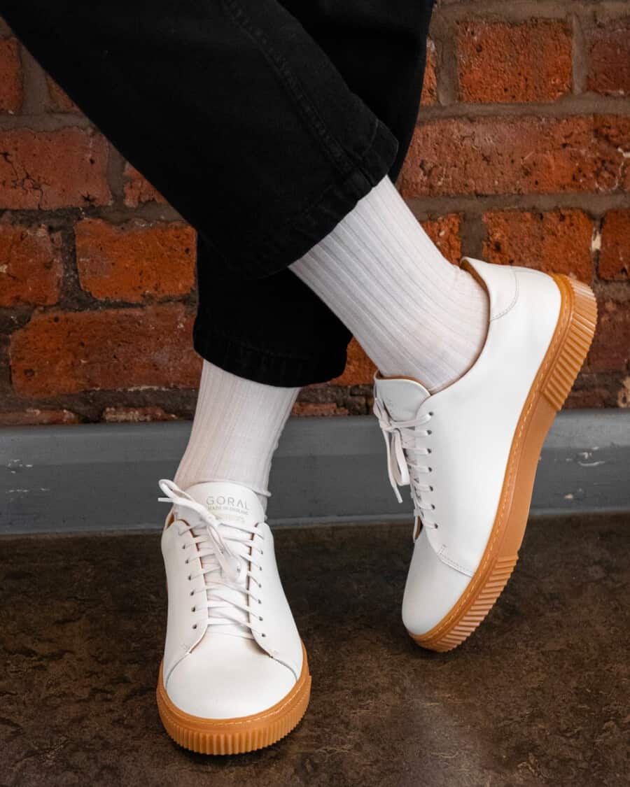 Man wearing luxury Goral white leather sneakers with a gum sole on feet with white socks and black sweatpants