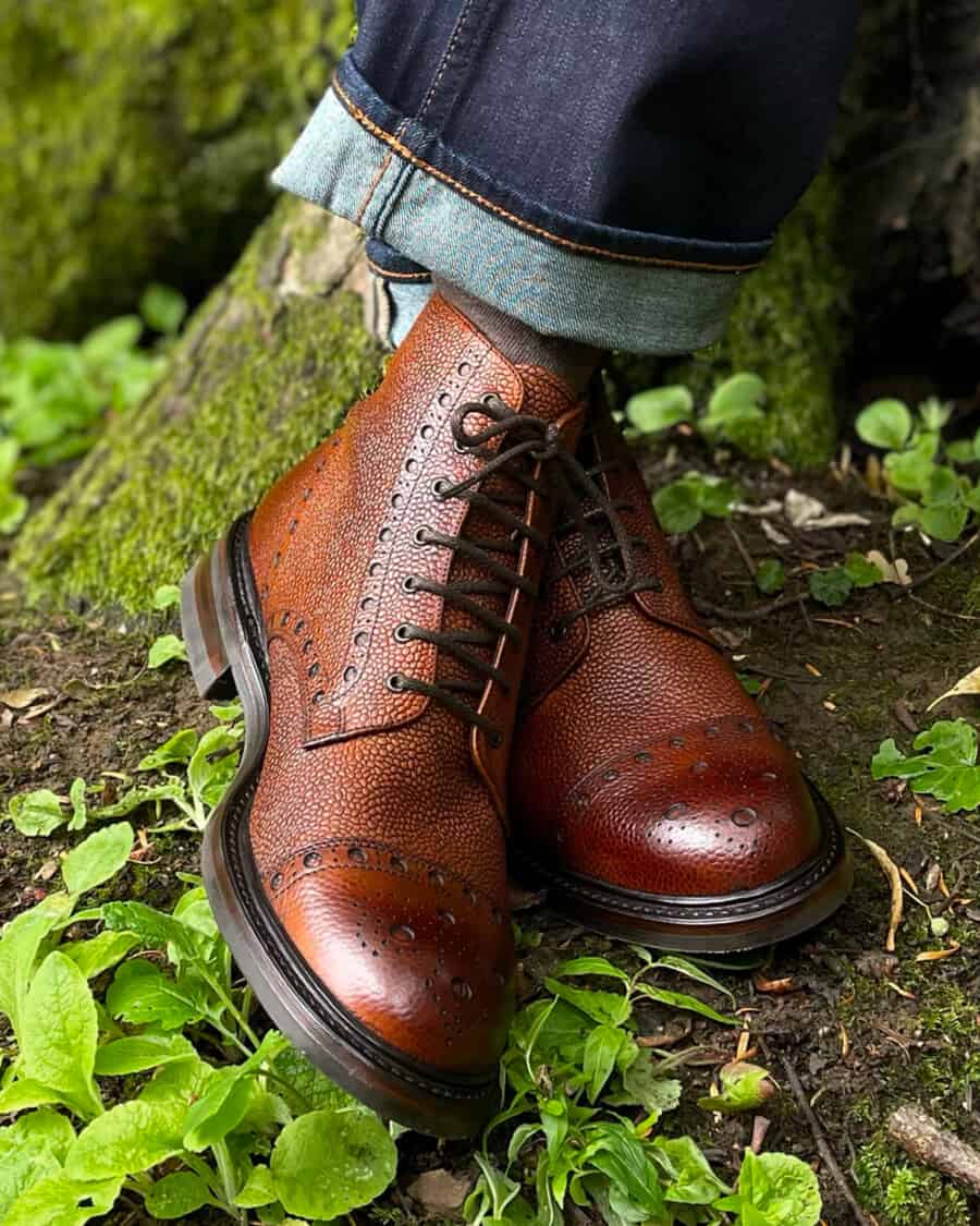 Men's brown pebble leather brogue boots by Loake worn on feet with raw selvage denim jeans