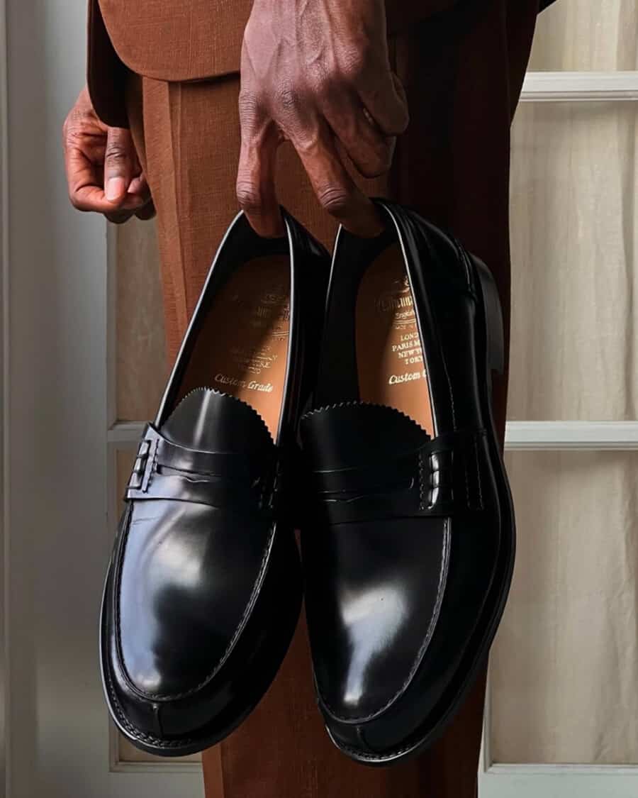 Man holding a pair of black leather British-made penny loafers by Church's