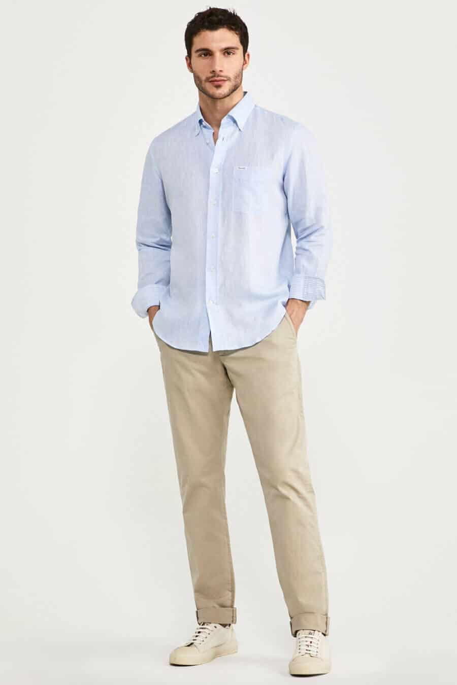 Men's khaki pants worn with a pale blue linen shirt and canvas sneakers outfit