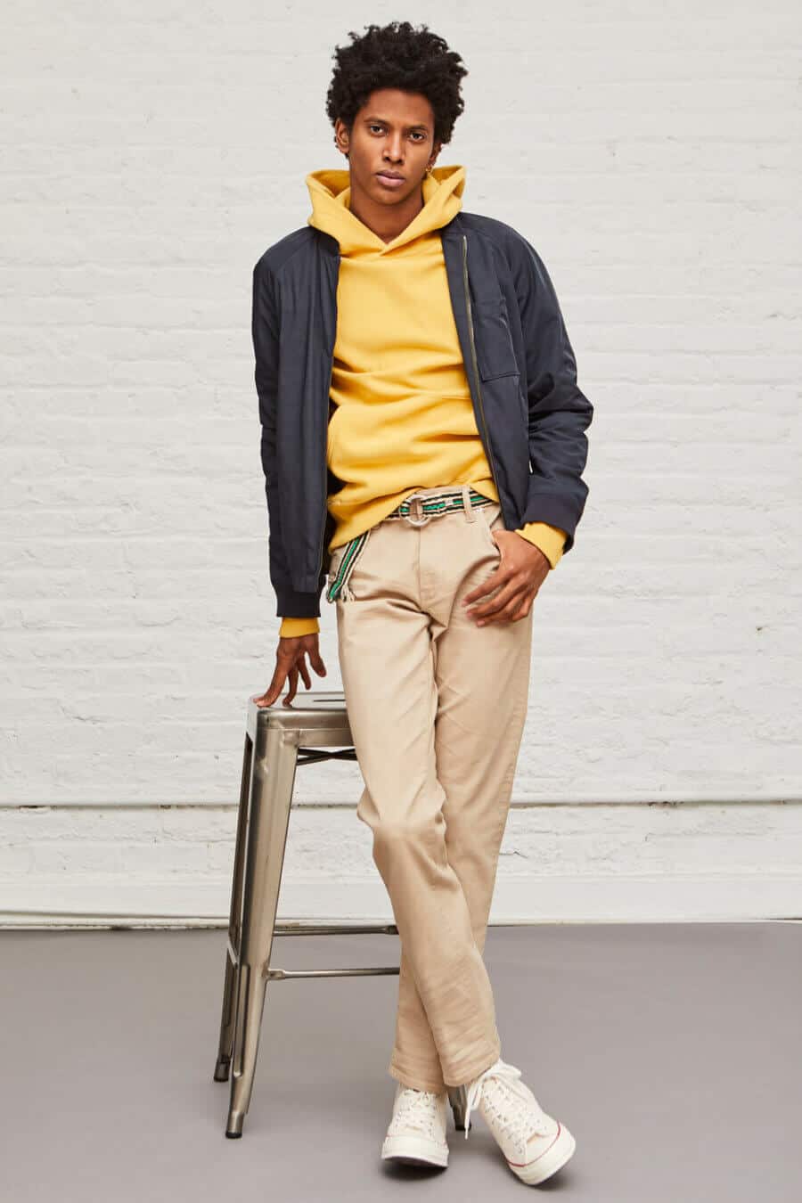 Men's khaki chinos worn with a yellow hoodie and navy bomber jacket outfit