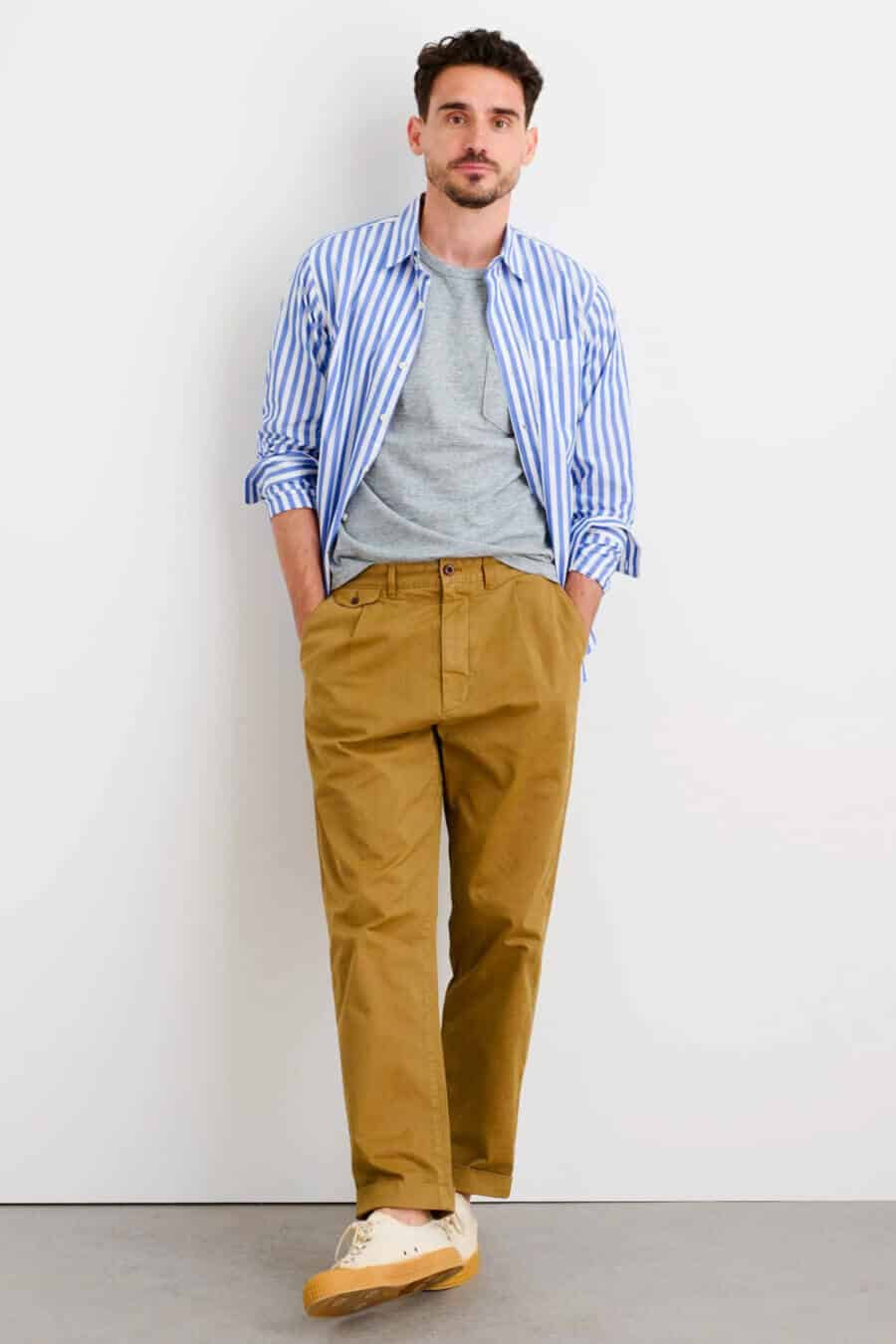 Men's wide khaki pants worn with a striped shirt and grey tee outfit