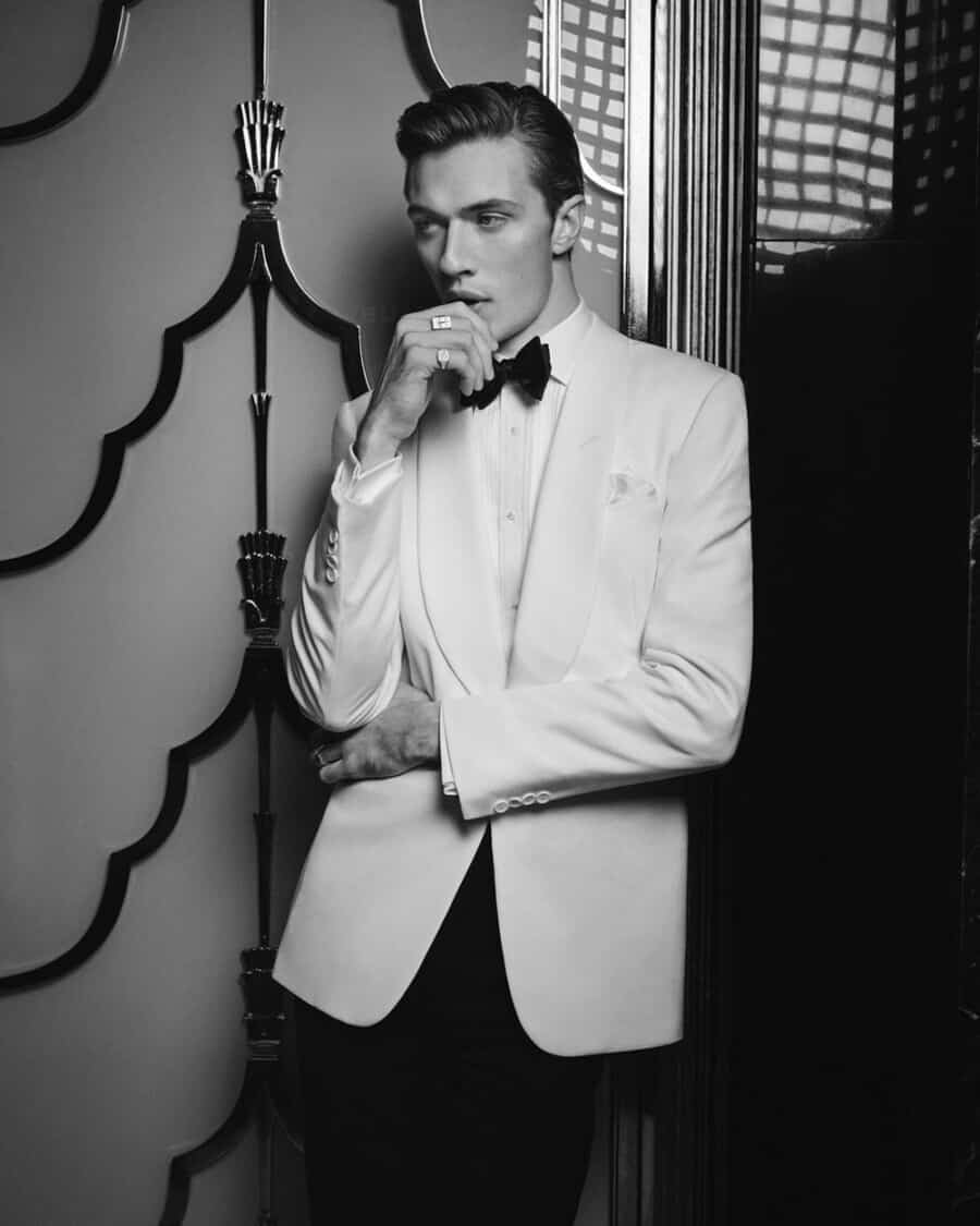 Male model Lucky Blue Smith wearing a white shawl lapel tuxedo jacket with a white dress shirt, black bow tie and black tuxedo pants