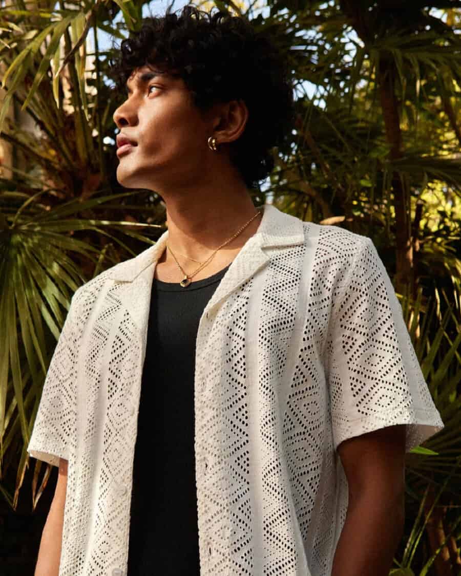 Man wearing a crochet Cuban collar shirt in white layered over a black vest