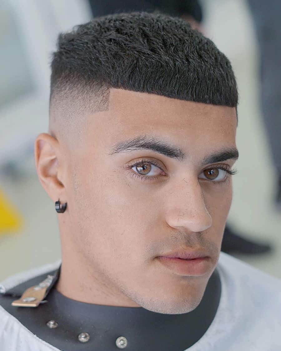 Short, sharp wavy haircut with a blunt fringe and high bald fade