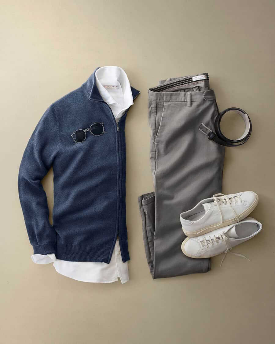 Men's grey chinos, white shirt, navy cashmere zip through cardigan and white sneakers flat lay outfit
