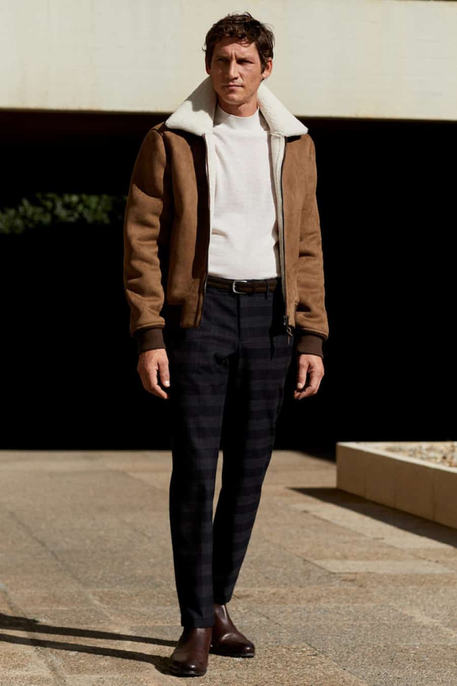 Men's dark checked trousers, brown leather chelsea boots, white roll neck and suede aviator jacket outfit