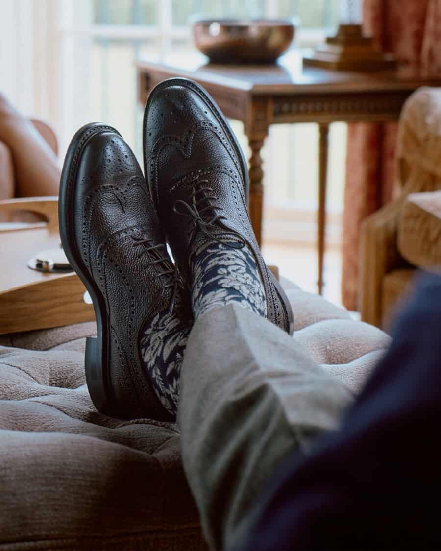 Men's Joseph Cheaney & Sons luxury Oxford brogues worn on feet with navy floral socks and grey wool pants