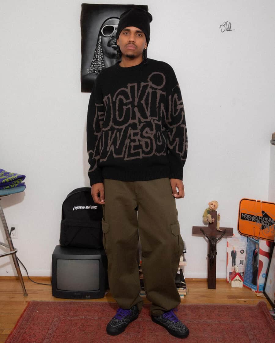 Man wearing f*cking awesome streetwear logo black sweater, olive green loose cargo pants, black sneakers and black beanie