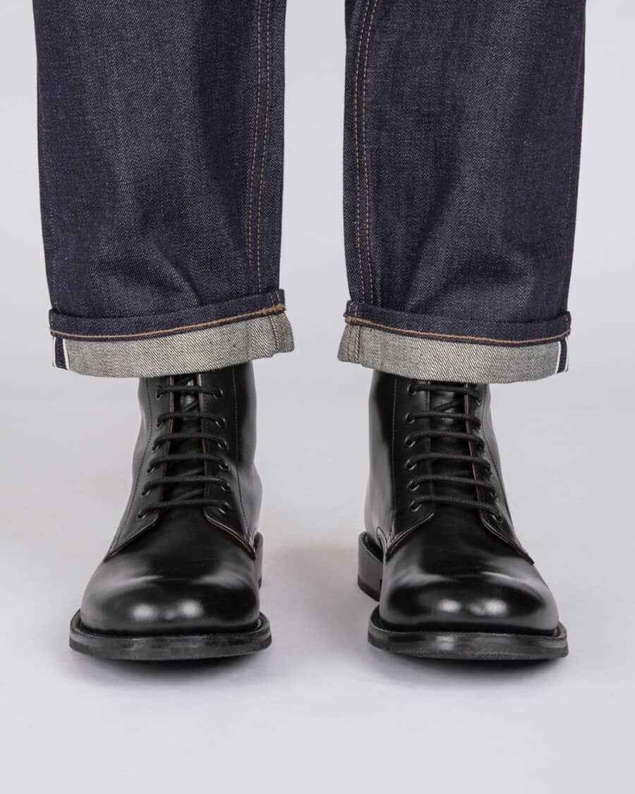 Men's black Grenson military boots worn on feet with raw denim selvage jeans
