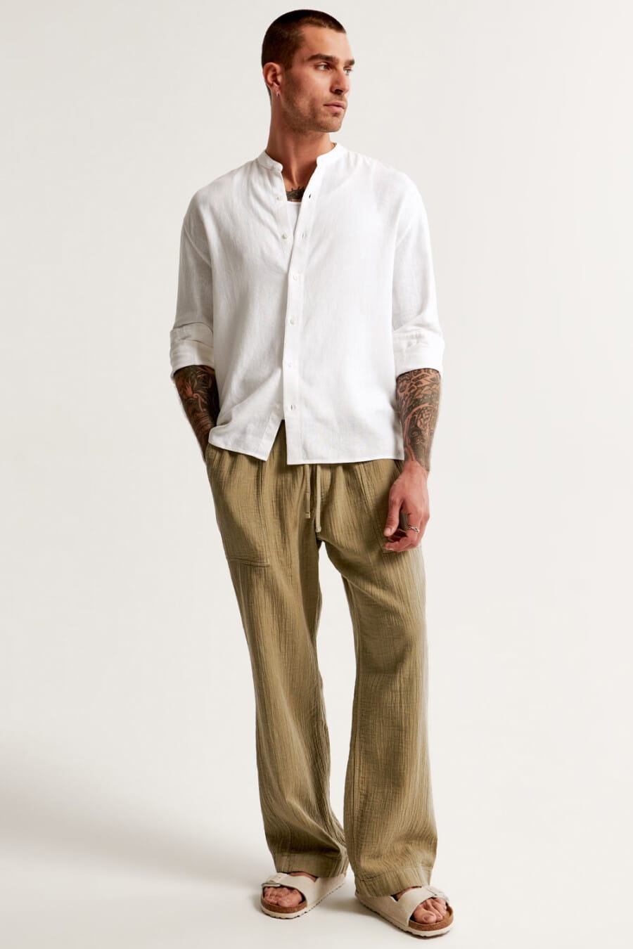 Men's loose khaki linen pants, white grandad/band collar shirt, white tank top and beige slider sandals outfit