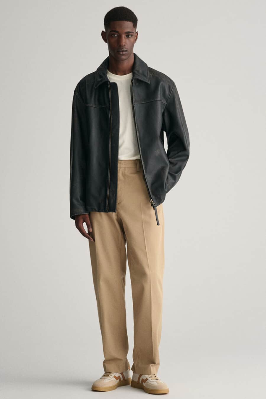 Men's wide leg kahki pants, tucked in white T-shirt, black collared leather jacket and beige/brown suede gum sole sneakers outfit