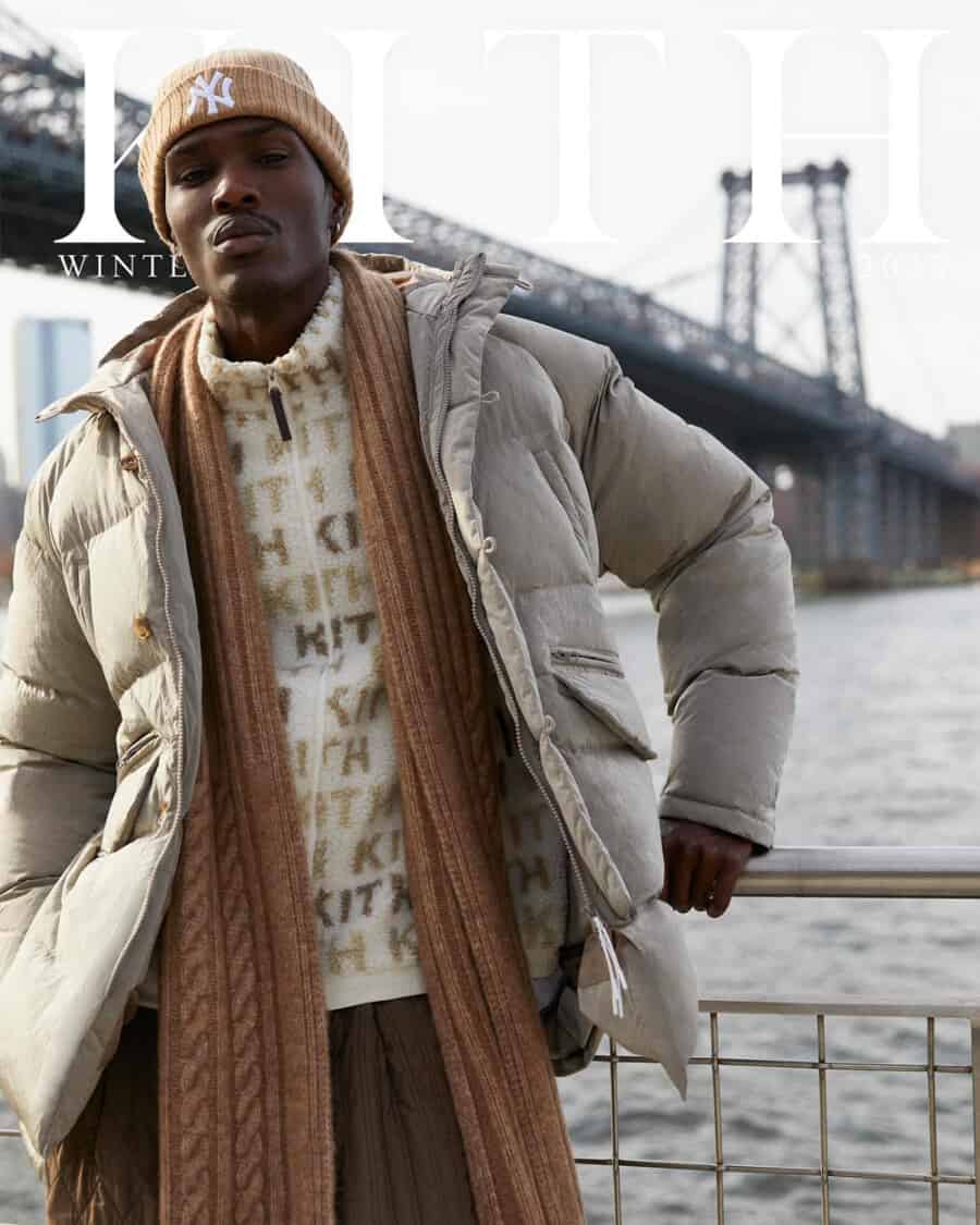 KITH Streetwear ad showing man wearing brown wide pants, Kith logo fleece, brown scarf, brown NY beanie and light grey puffer jacket
