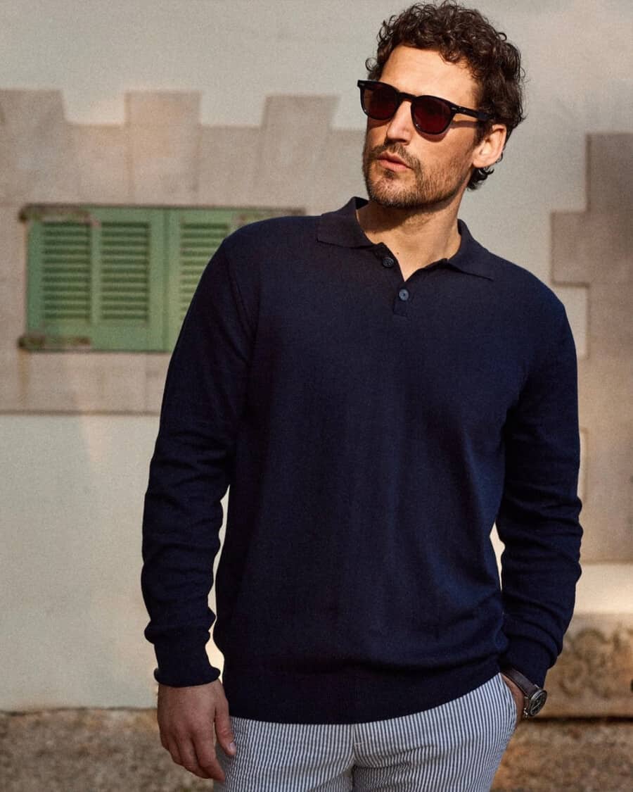 Man wearing a long sleeve blue knitted polo shirt with striped shorts and sunglasses