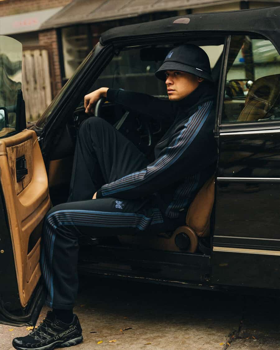 Man sitting in car wearing Needles x Haven matching streetwear tracksuit and bucket hat