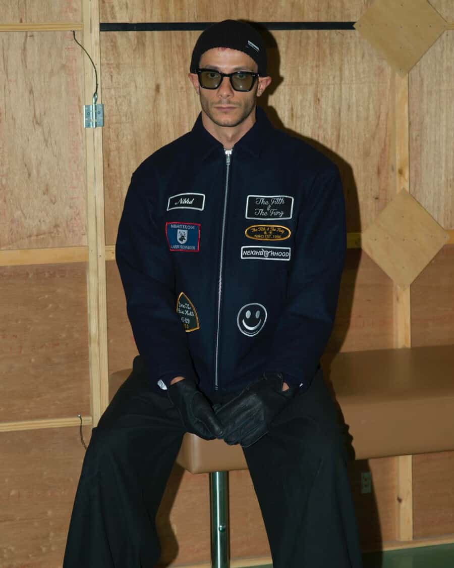 Man wearing Neighborhood Japan streetwear patch jacket, baggy black pants and black beanie