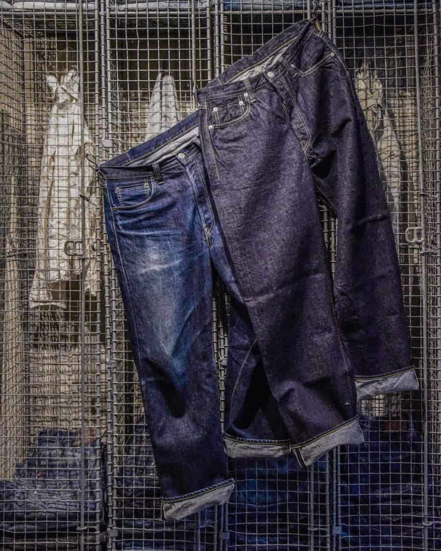 A pair of raw and washed denim jeans hanging on a wire frame