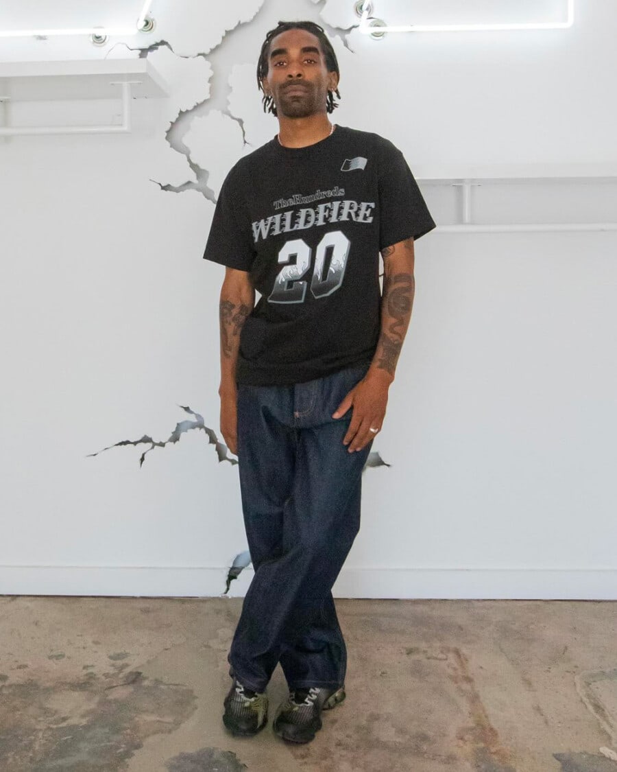 Man wearing The Hundreds streetwear black printed T-shirt, raw denim jeans and black sneakers