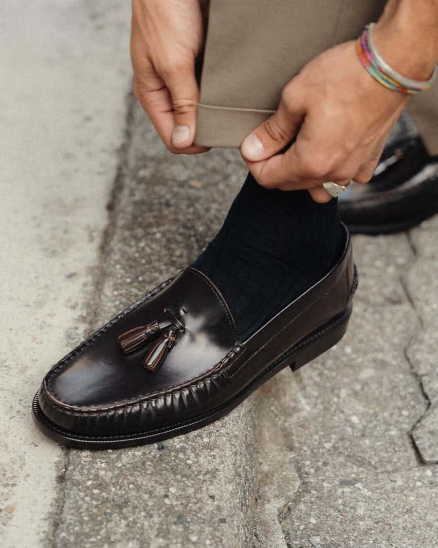 Man wearing brown leather ITalian tassel loafers on feet with navy socks and brown turn up pants