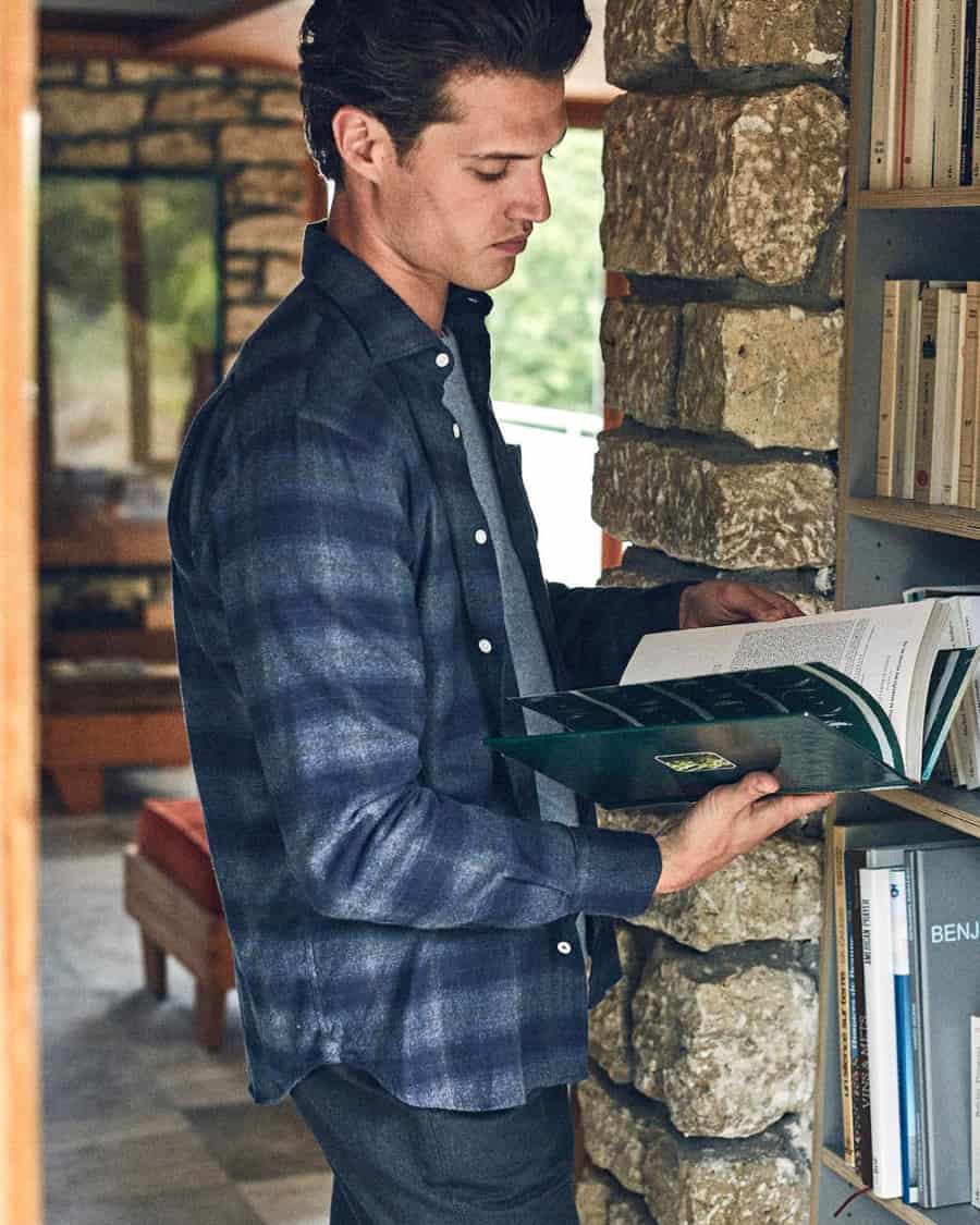 Man wearing a blue checked flannel shirt reading a book