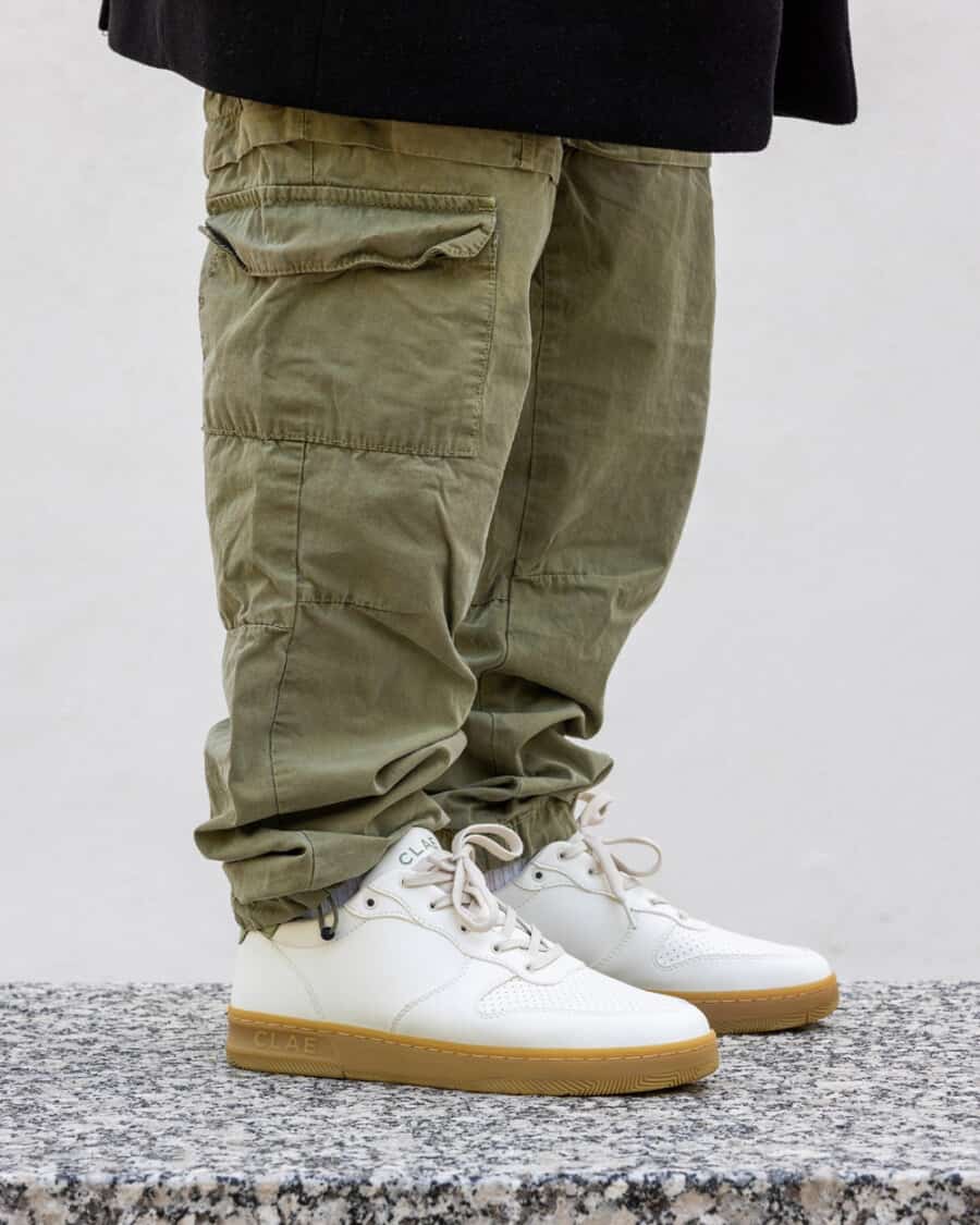 Man wearing Clae Malone white with gum sole minimalist sneakers on feet with green cargo pants and oversized black T-shirt