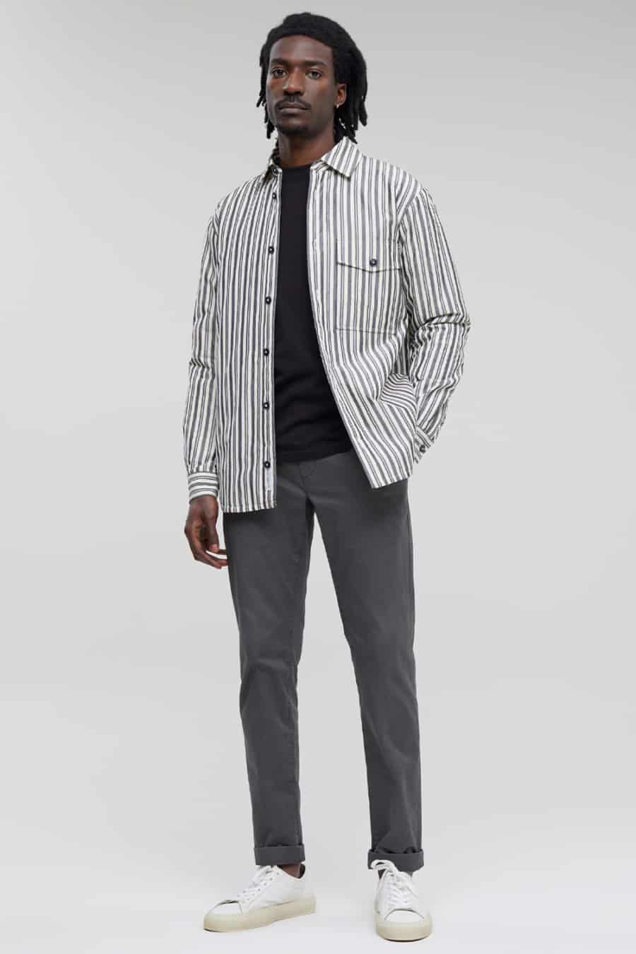 Men's grey chinos, black T-shirt, striped overshirt and white sneakers outfit
