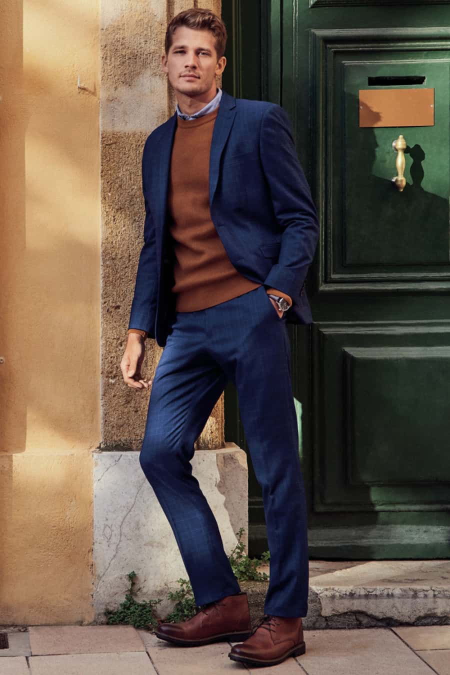 Men's mid-blue suit, brown sweater and brown leather chukka boots outfit