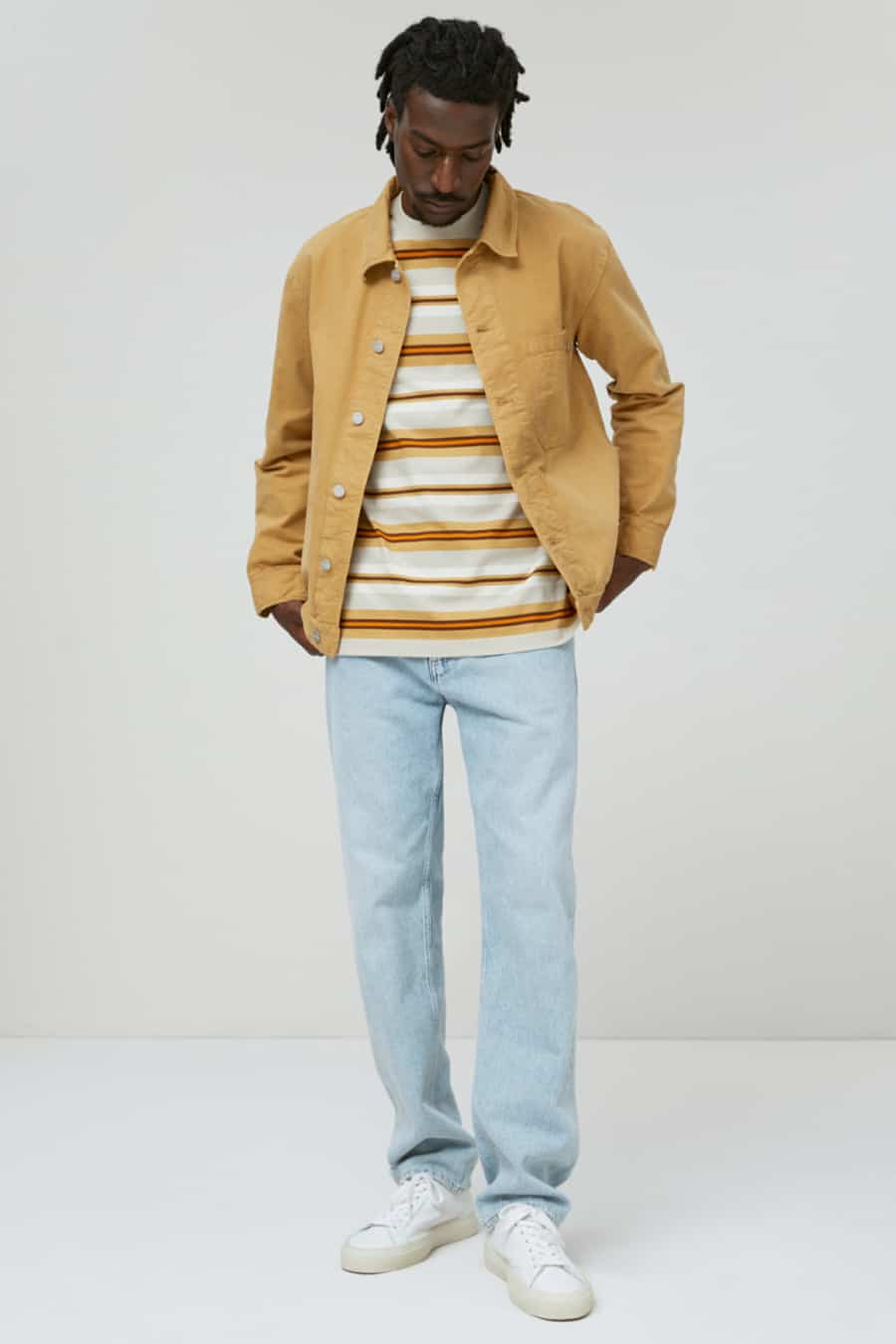 Men's pale wash denim jeans, striped T-shirt, yellow overshirt and white sneakers outfit