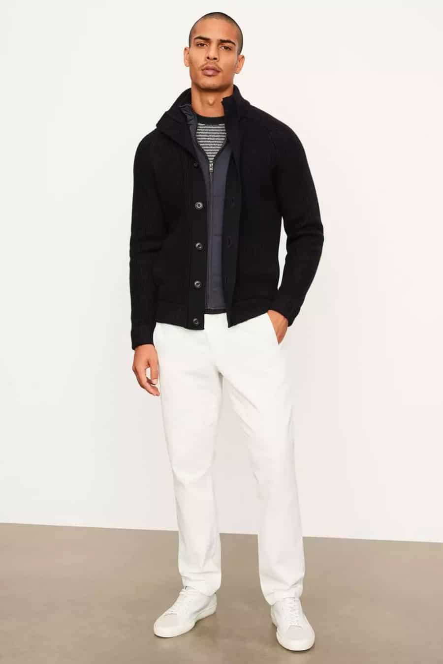 Men's white pants, black bodywarmer, black chunky knit cardigan and white sneakers outfit