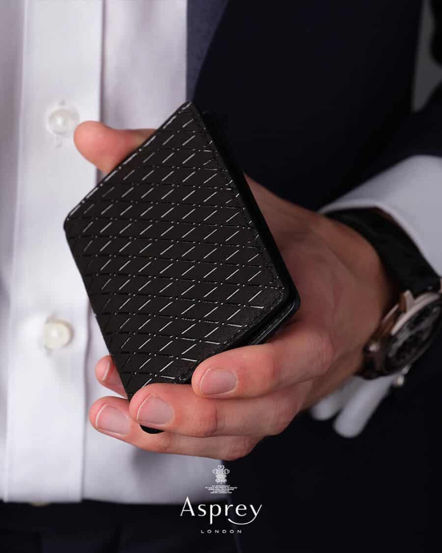 Man in tuxedo holding a black luxury leather wallet by Asprey London